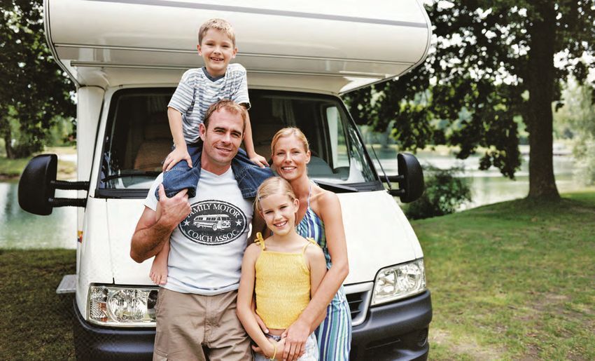 Family posing in front of a white RV; father with a child on his shoulders, mother and another child smiling.
