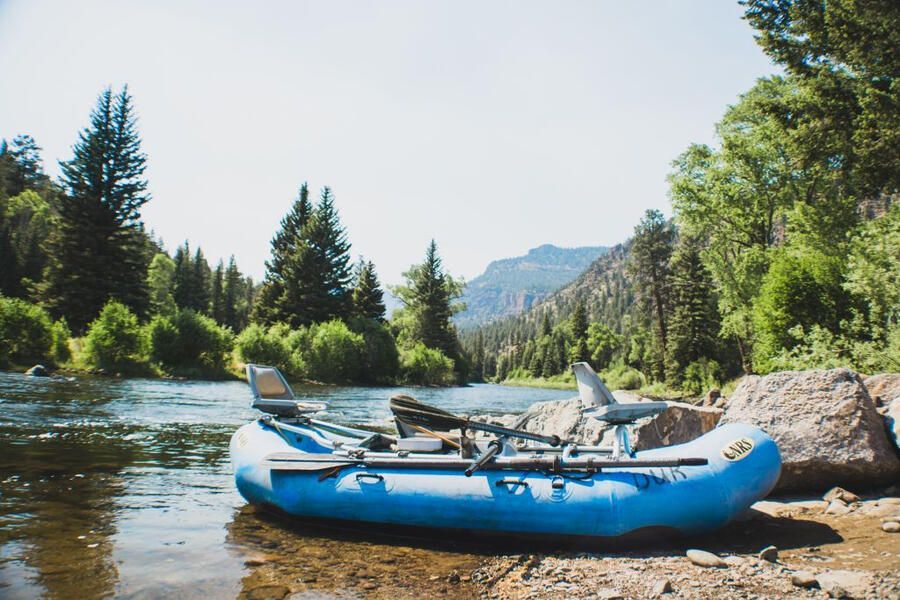 A blue raft is sitting on the shore of a river.