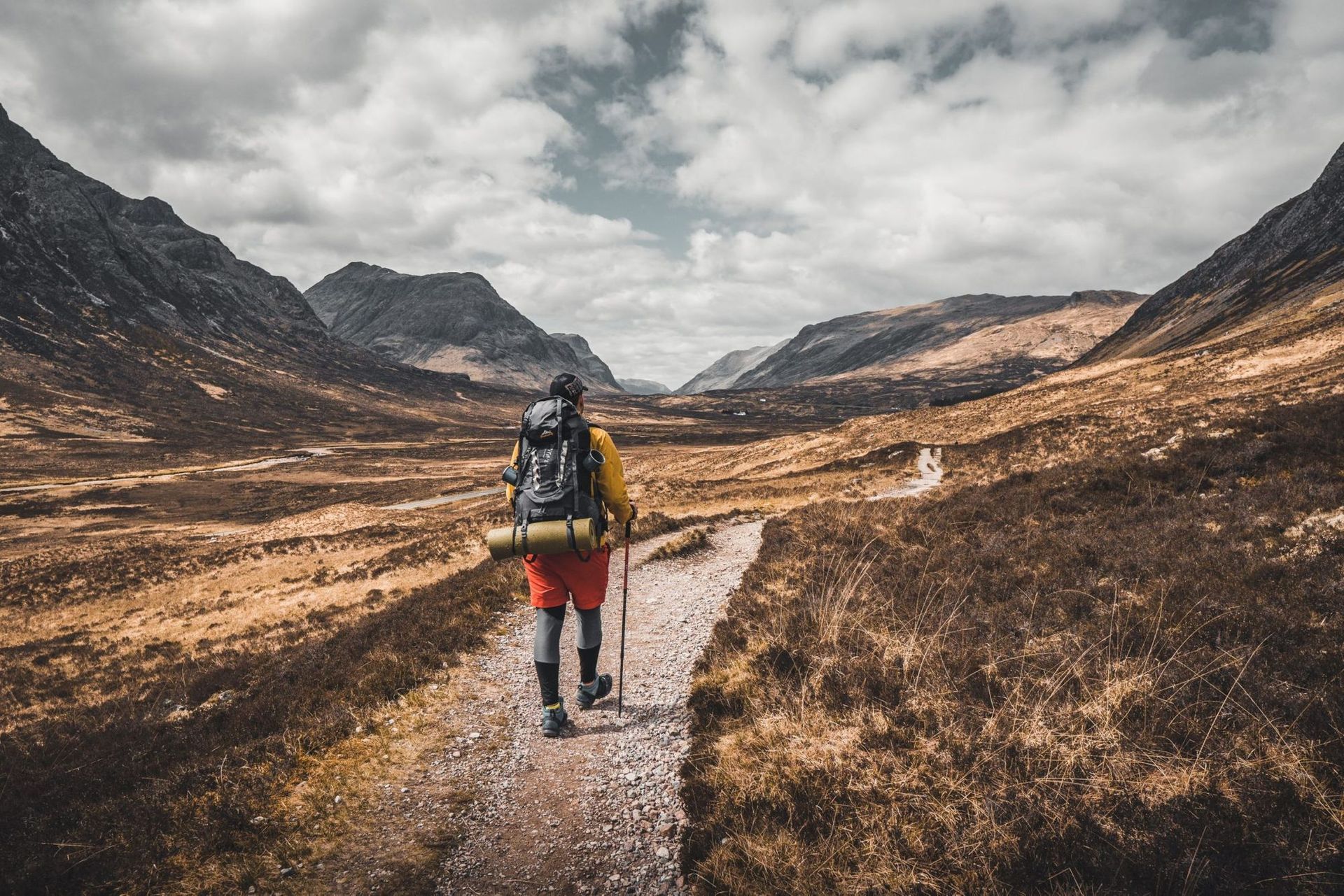 A person with a backpack is walking down a path in the mountains.