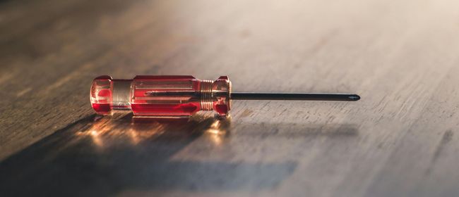 Red-handled screwdriver on a wood surface, lit by light coming from the left.