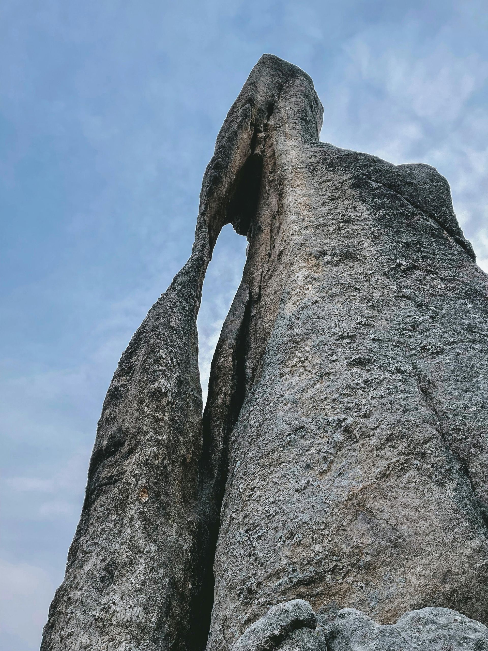 Rock formation arching against a cloudy sky. Gray and tan stone texture.