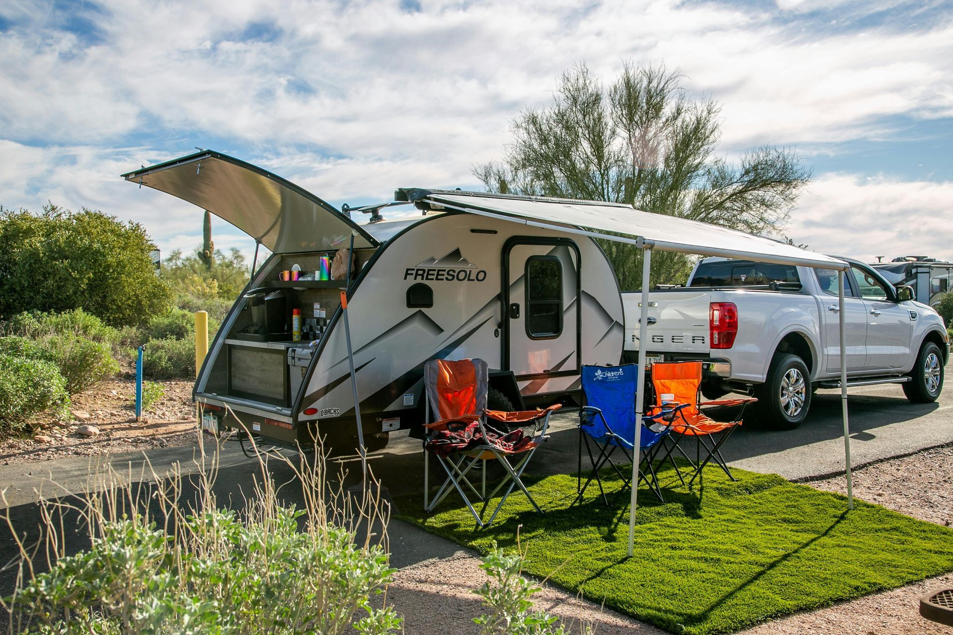 Small teardrop camper with open hatch and awning set up next to a white pickup truck.