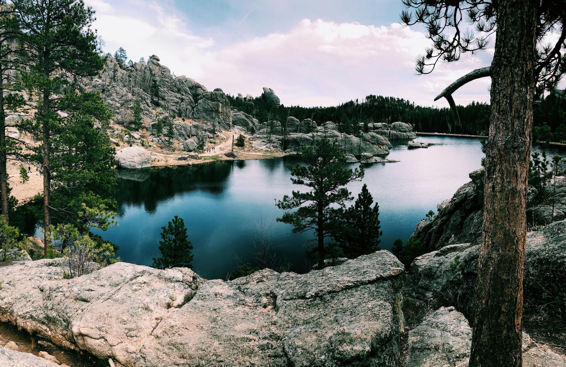 Lake surrounded by rocky cliffs and trees under a cloudy sky.