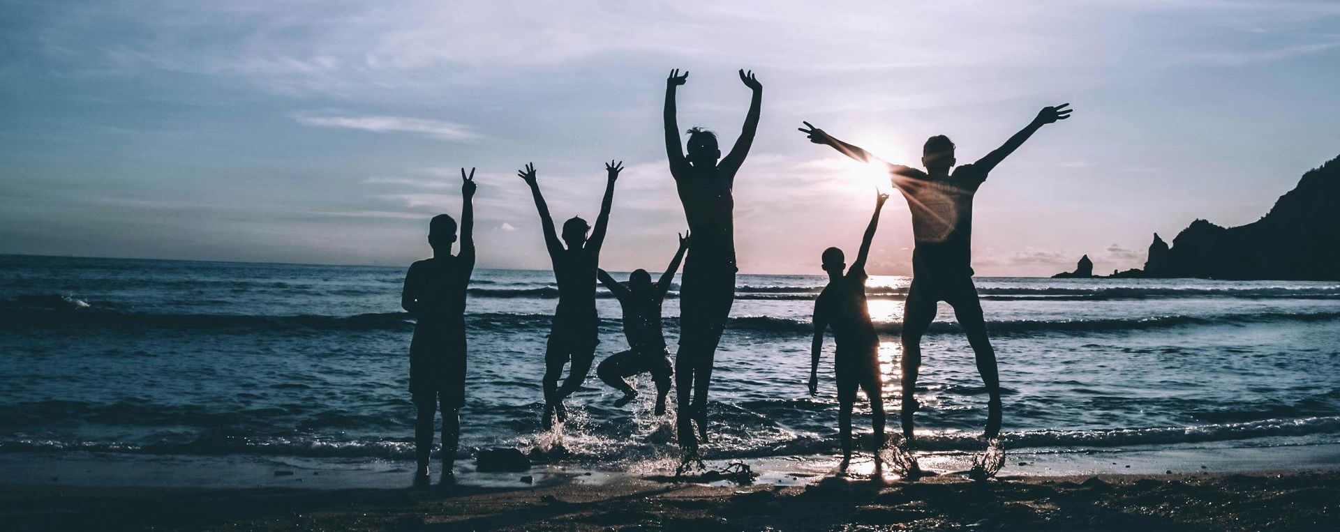 A group of people are jumping in the air on a beach at sunset.