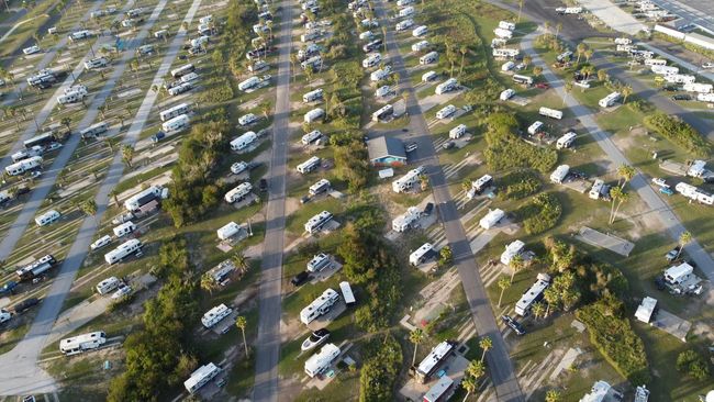 Aerial view of an RV park with numerous RVs parked on plots with trees and grass.