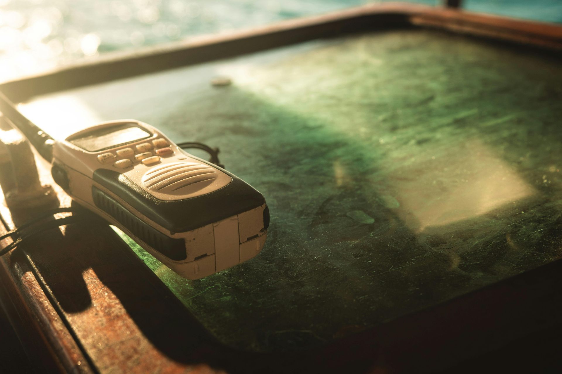 Handheld radio on a table, sunlight shining on water or glass below.