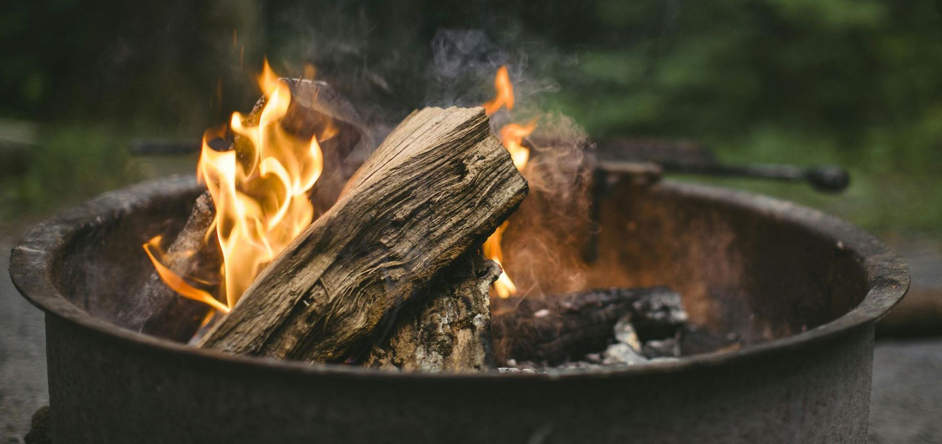 Campfire burning in a metal fire pit with flames and smoke, set outdoors.