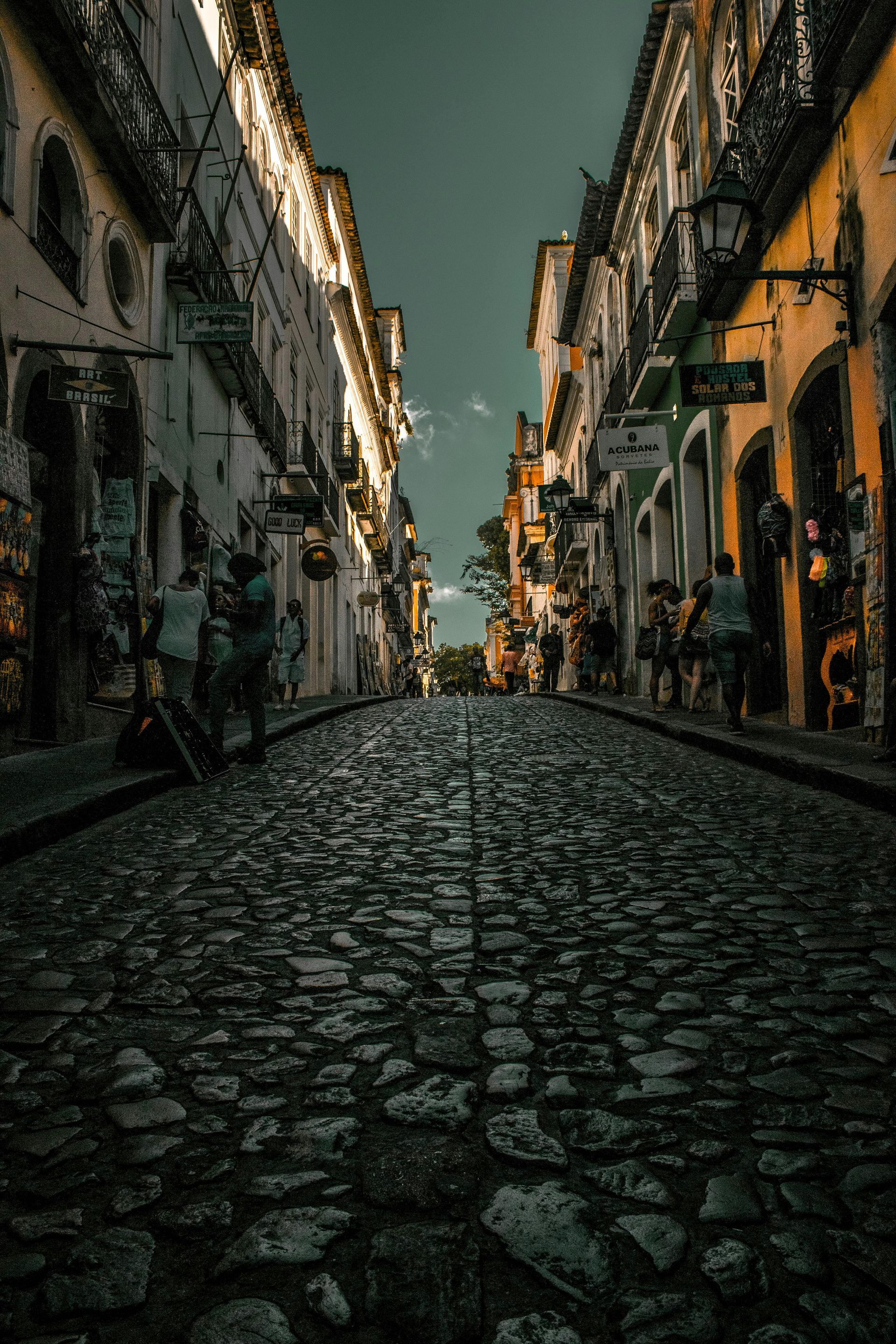 Cobblestone street in old city lined by buildings, pedestrians.