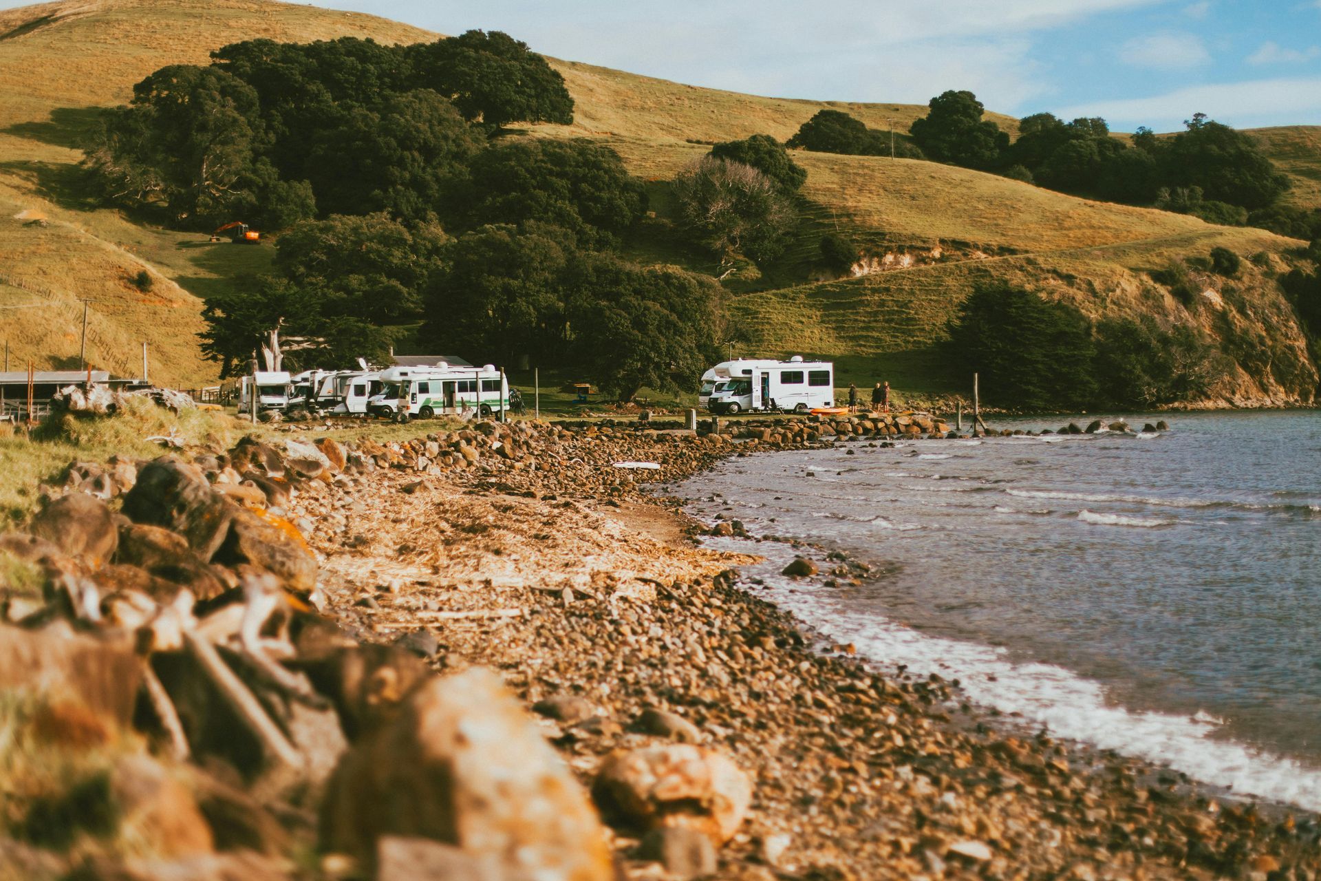 Rocky beach with parked RVs beneath green hills beside calm water