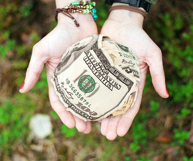 Hands holding a crumpled ball of U.S. dollar bills outdoors.