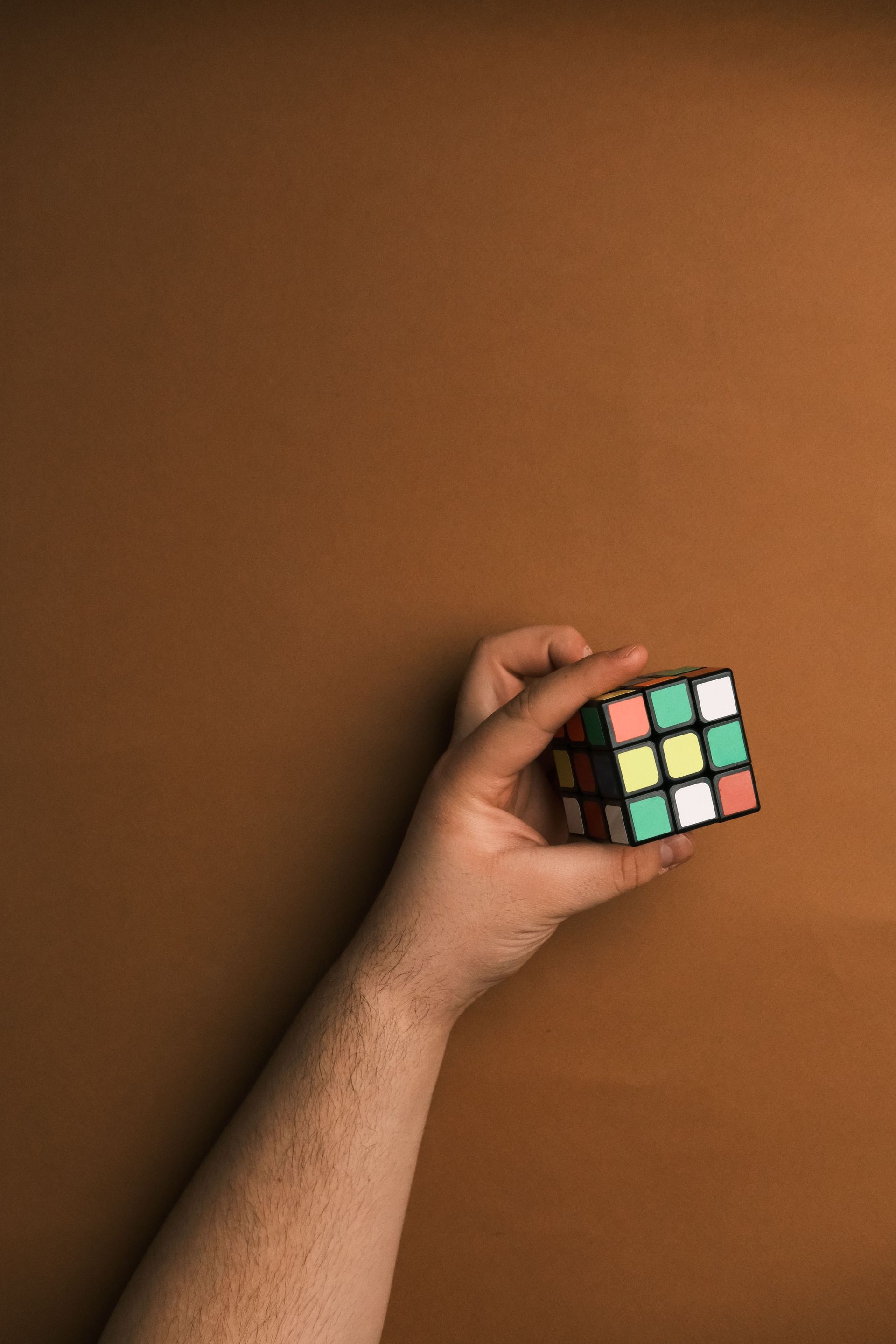Hand holding a scrambled Rubik’s cube against a plain brown background