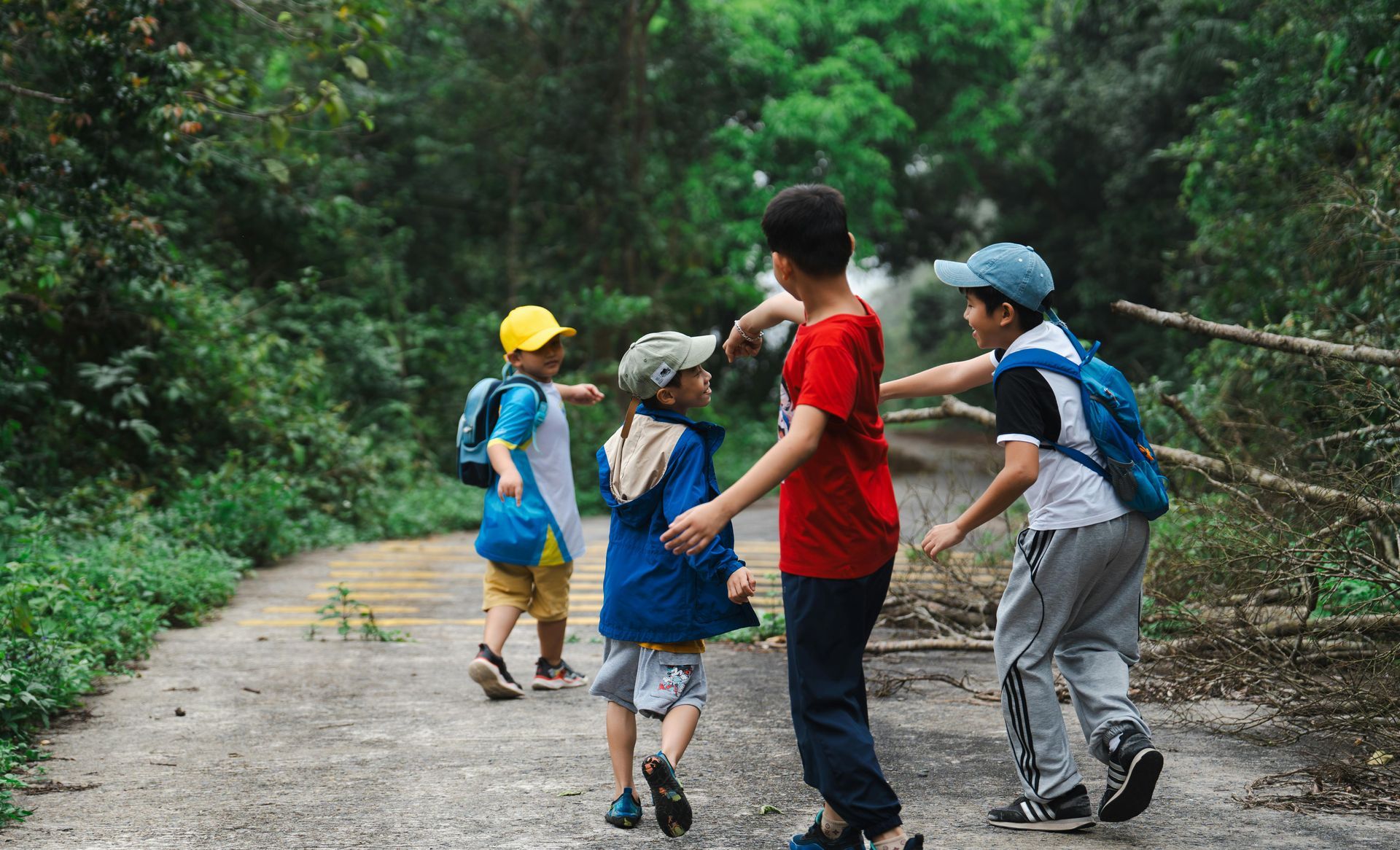Four children walking along a path in a forest. One boy in red shirt interacts with others.