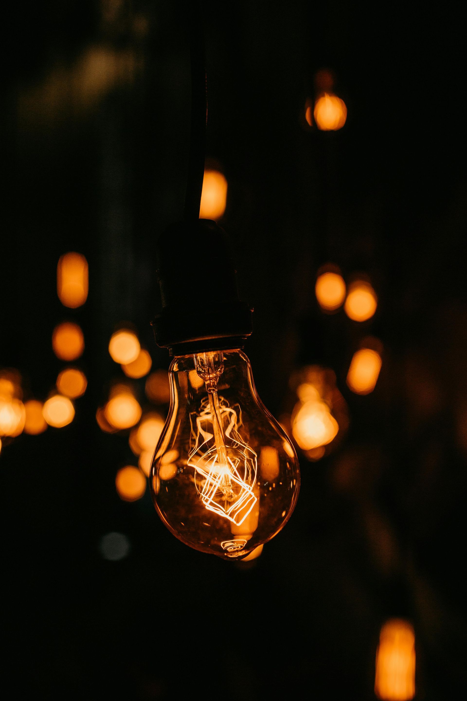 Glowing lightbulb hanging, others blurred in the dark, warm orange tones.