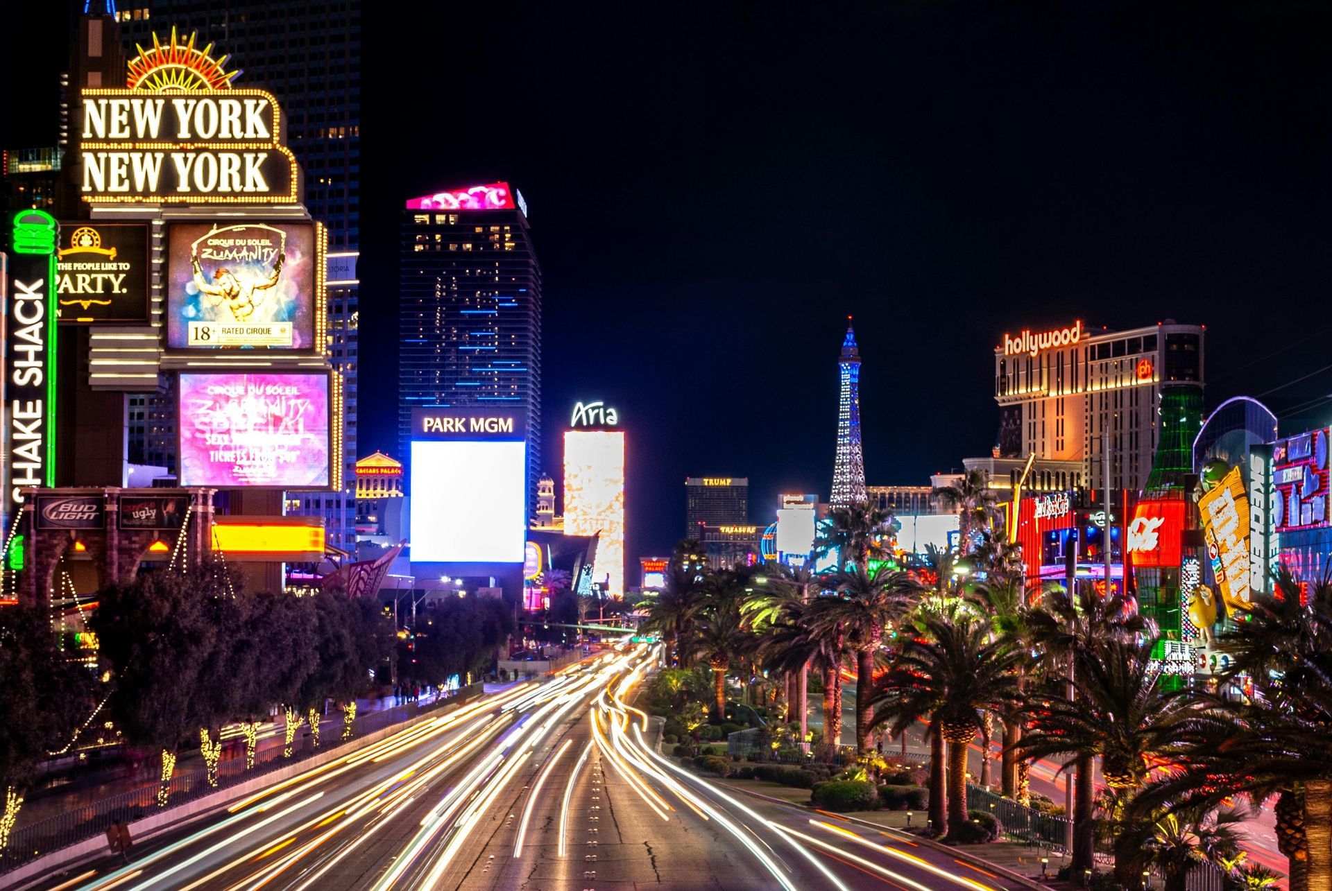Neon-lit Las Vegas Strip at night with traffic light trails and the Eiffel Tower in the distance