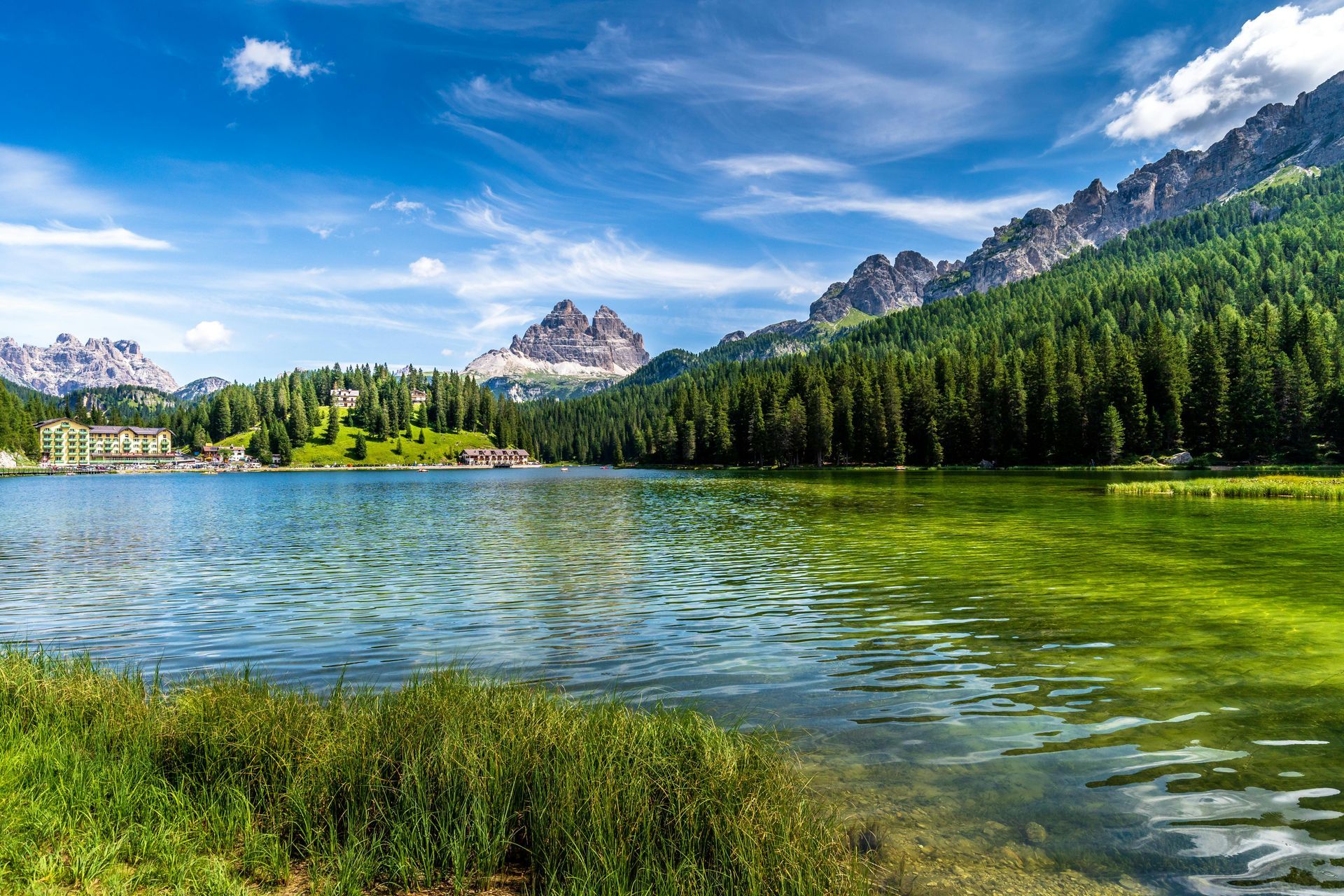 Lake Misurina in the Italian Dolomites, with green water, evergreen trees, mountains, and a blue sky.