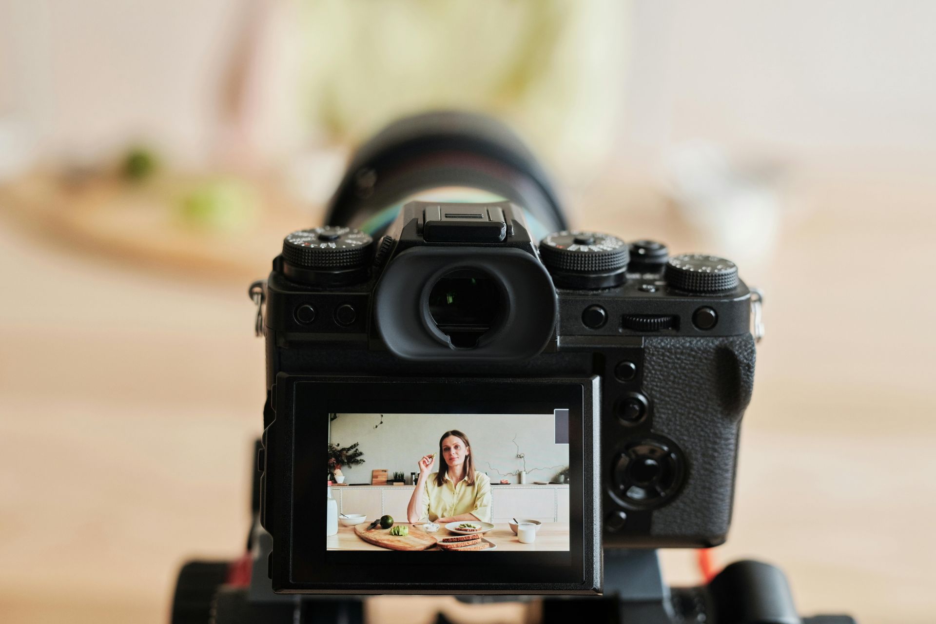 Camera filming a woman in a kitchen; she is talking while holding something and appears to be filming a cooking show.