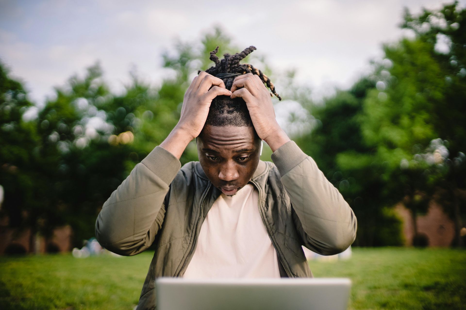 A man is sitting in front of a laptop computer with his hands on his head.