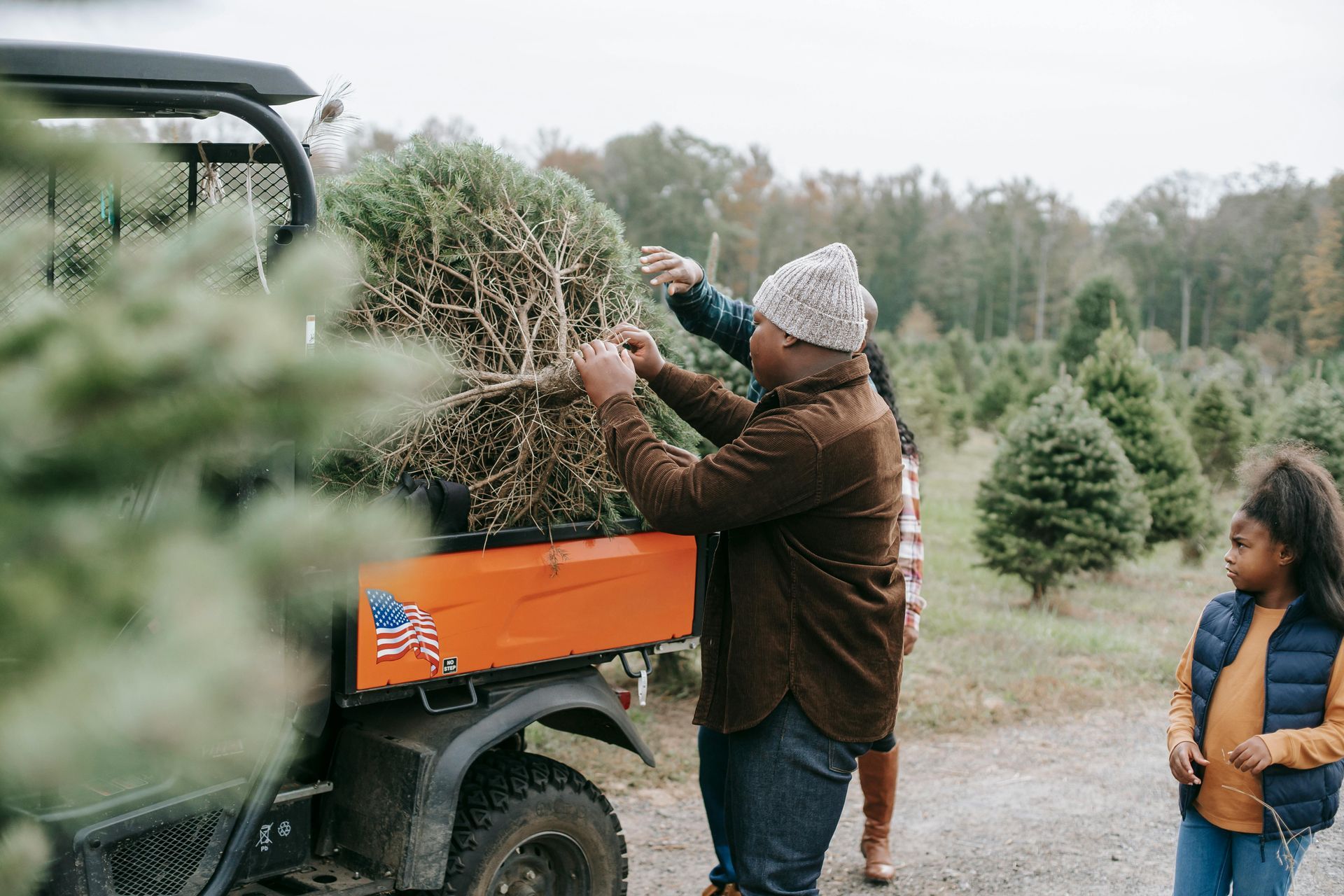 Family loading Christmas tree onto utility vehicle at a tree farm.