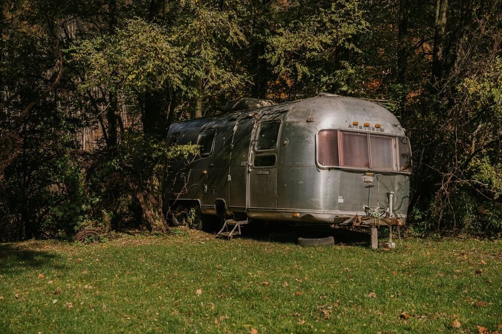 Silver Airstream trailer in a grassy area, partially obscured by trees and foliage.