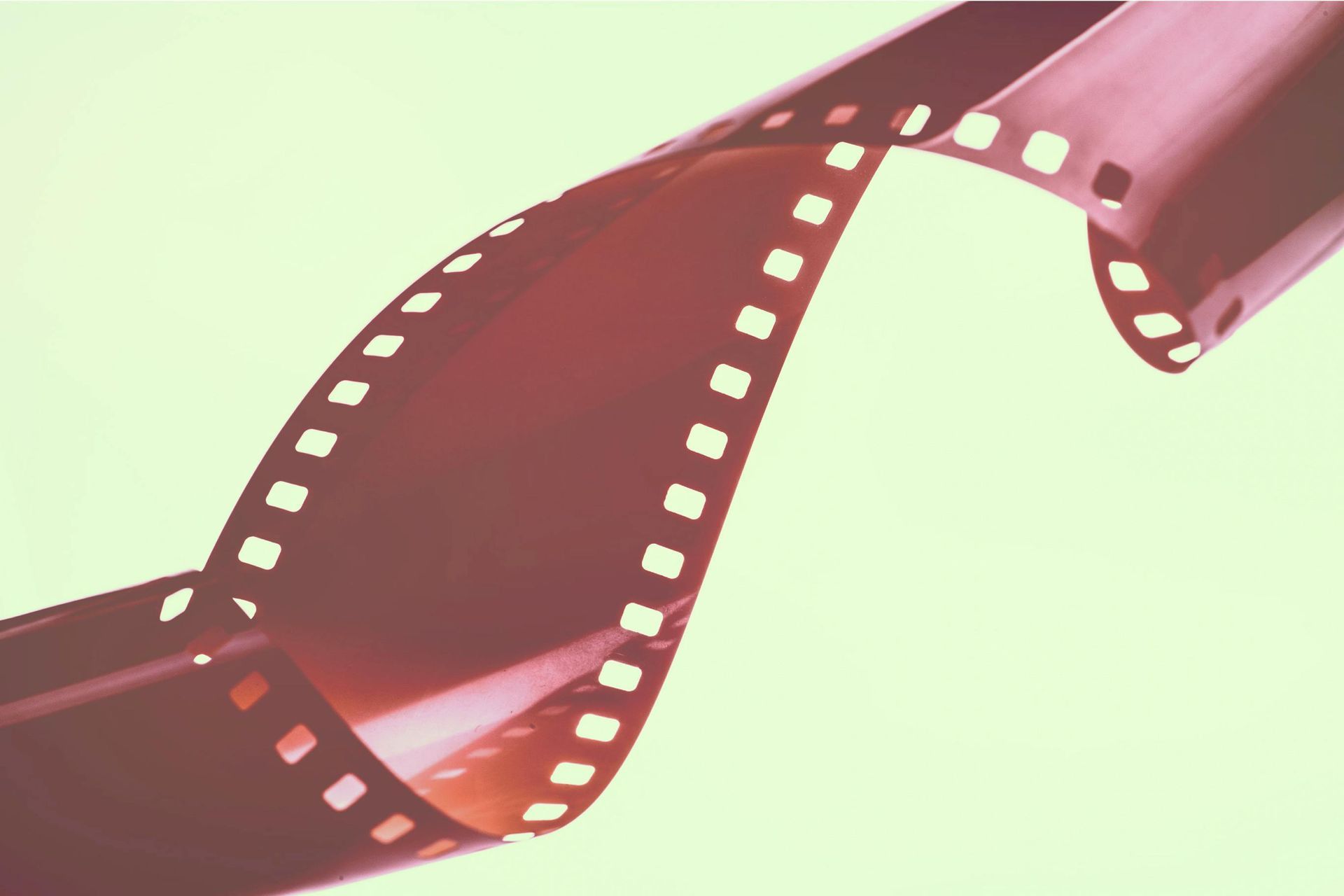 Curled strip of red film against a light yellow background, showing sprocket holes.