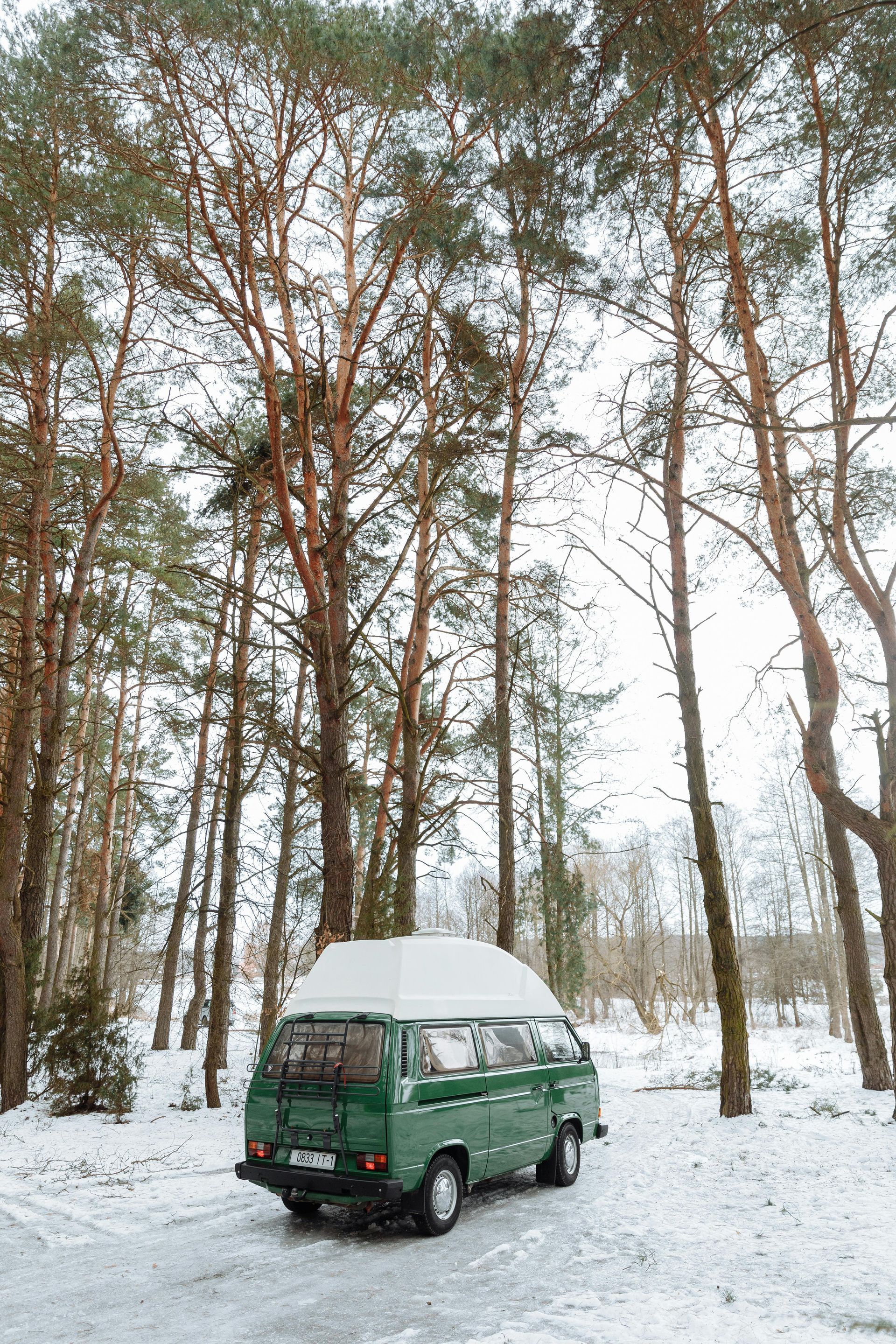 Green campervan parked in a snowy forest.