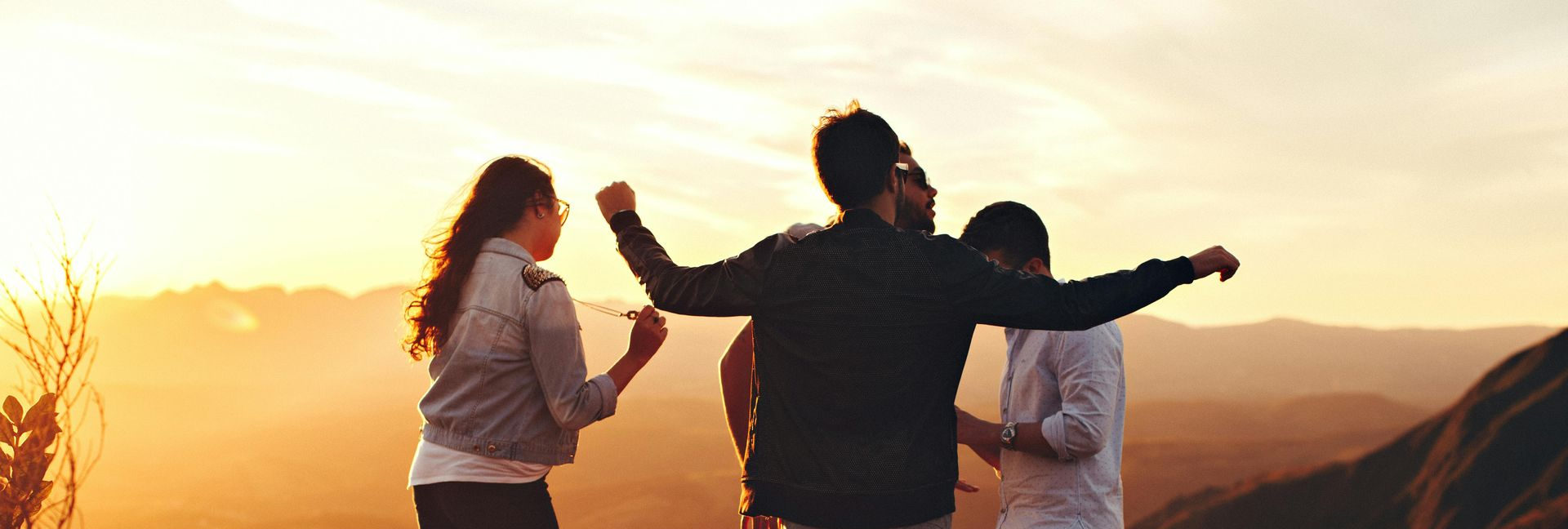 Three people on a hilltop with arms raised towards the sunset.