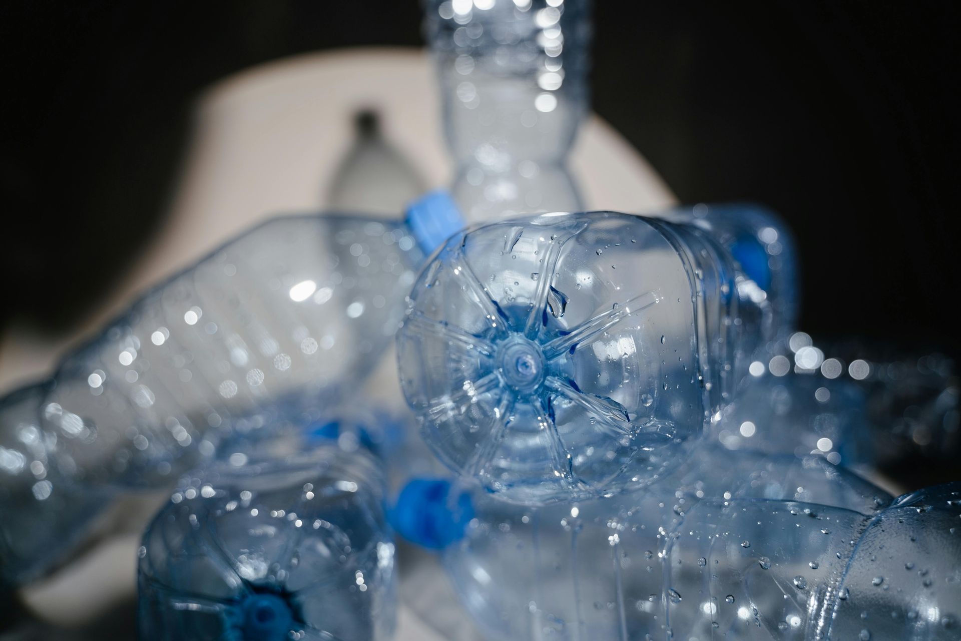 Pile of clear plastic water bottles with blue caps, some in focus.