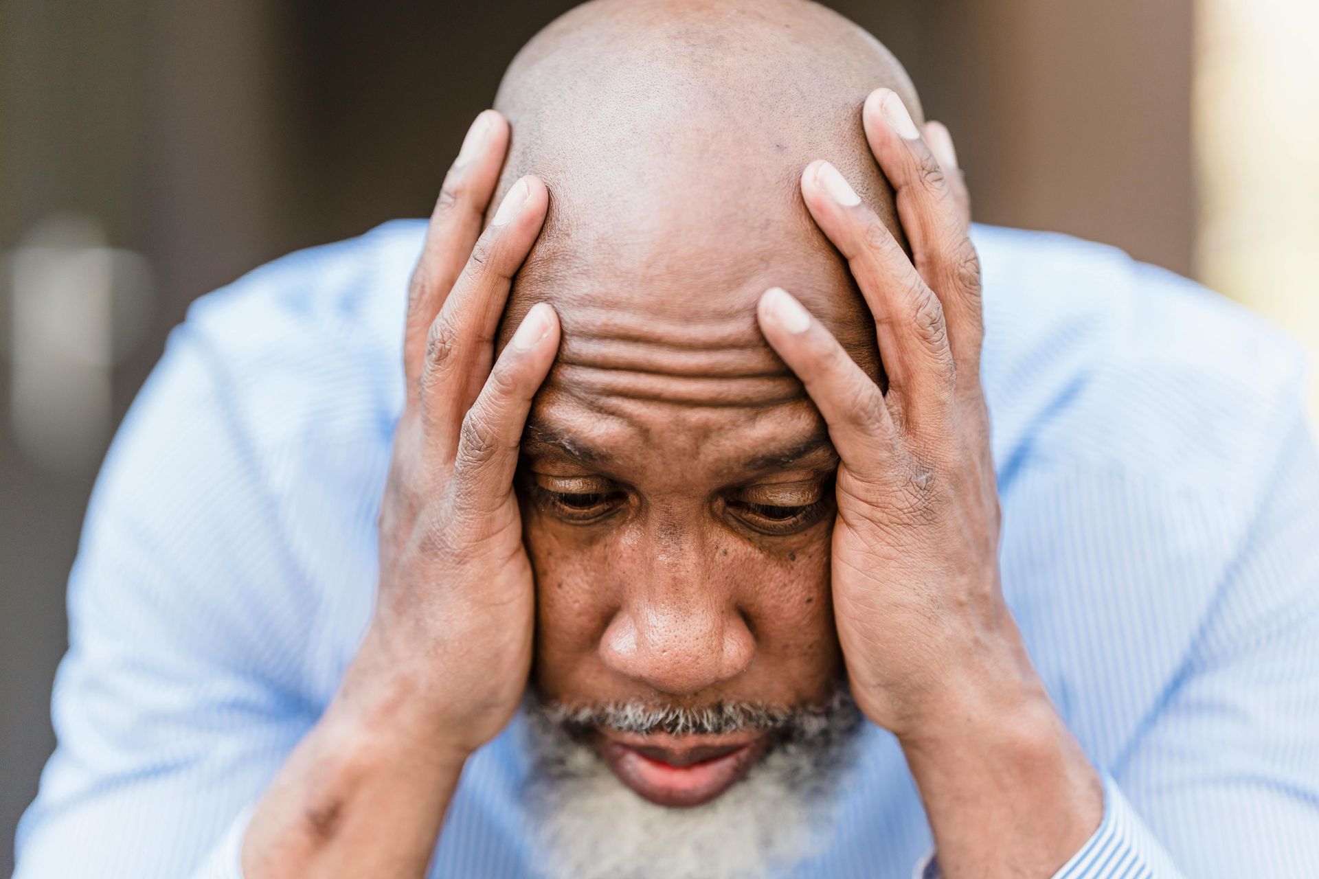 A bald man with a beard is holding his head in his hands.