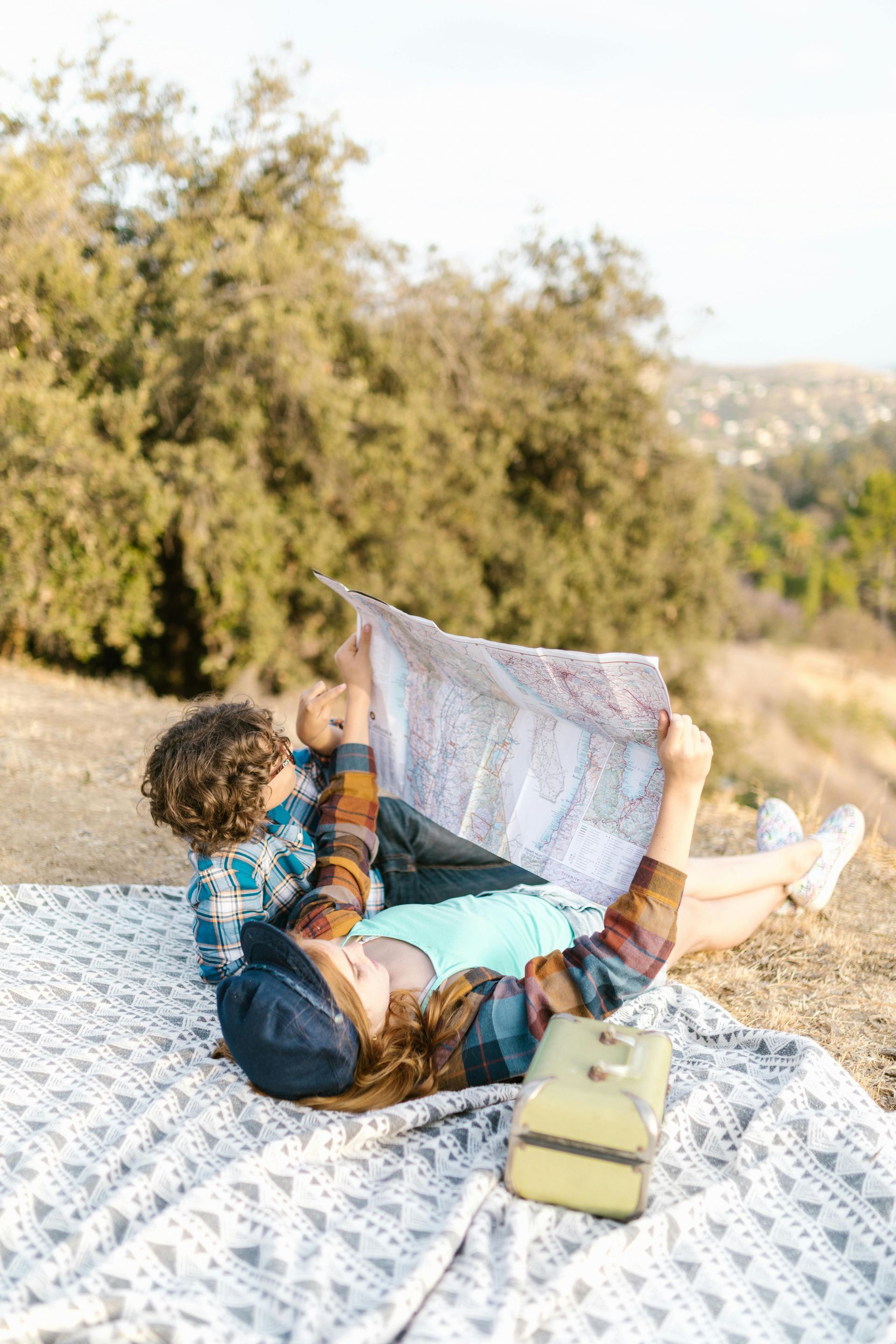 A man and a woman are laying on a blanket looking at a map.