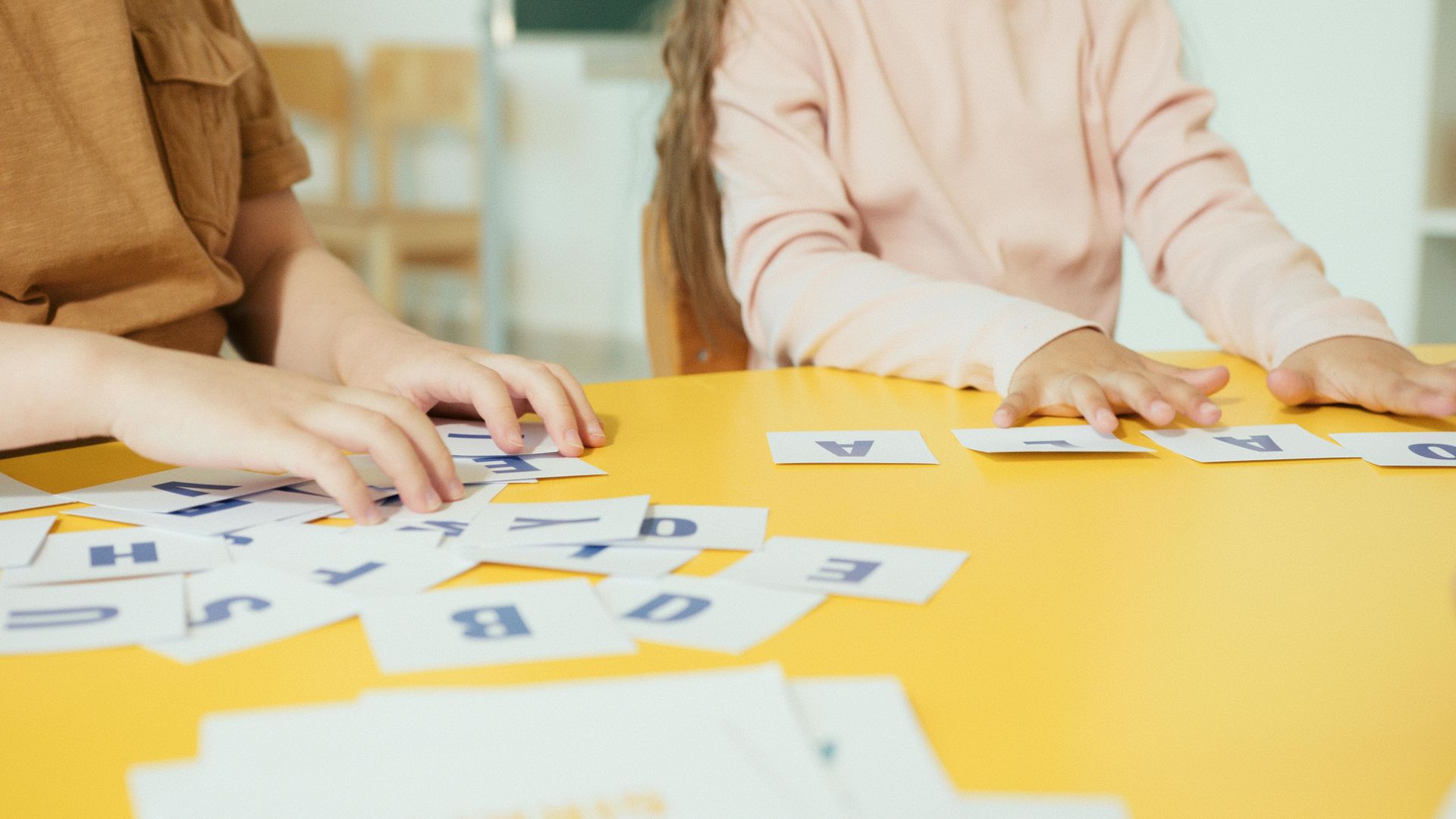 Hands arranging letter cards on a yellow table during a group learning activity
