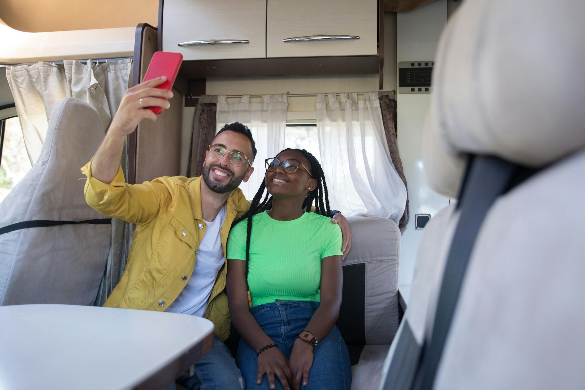 Couple taking a selfie inside a campervan. The man holds up a red phone, smiling. The woman looks up smiling.
