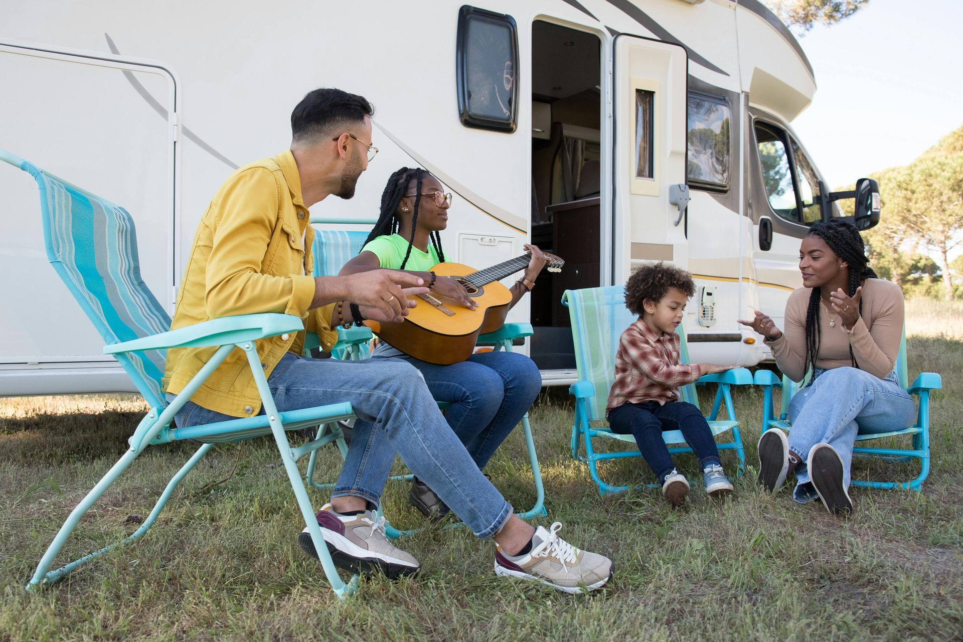 Family outside RV; woman playing guitar, others seated in chairs, clapping.