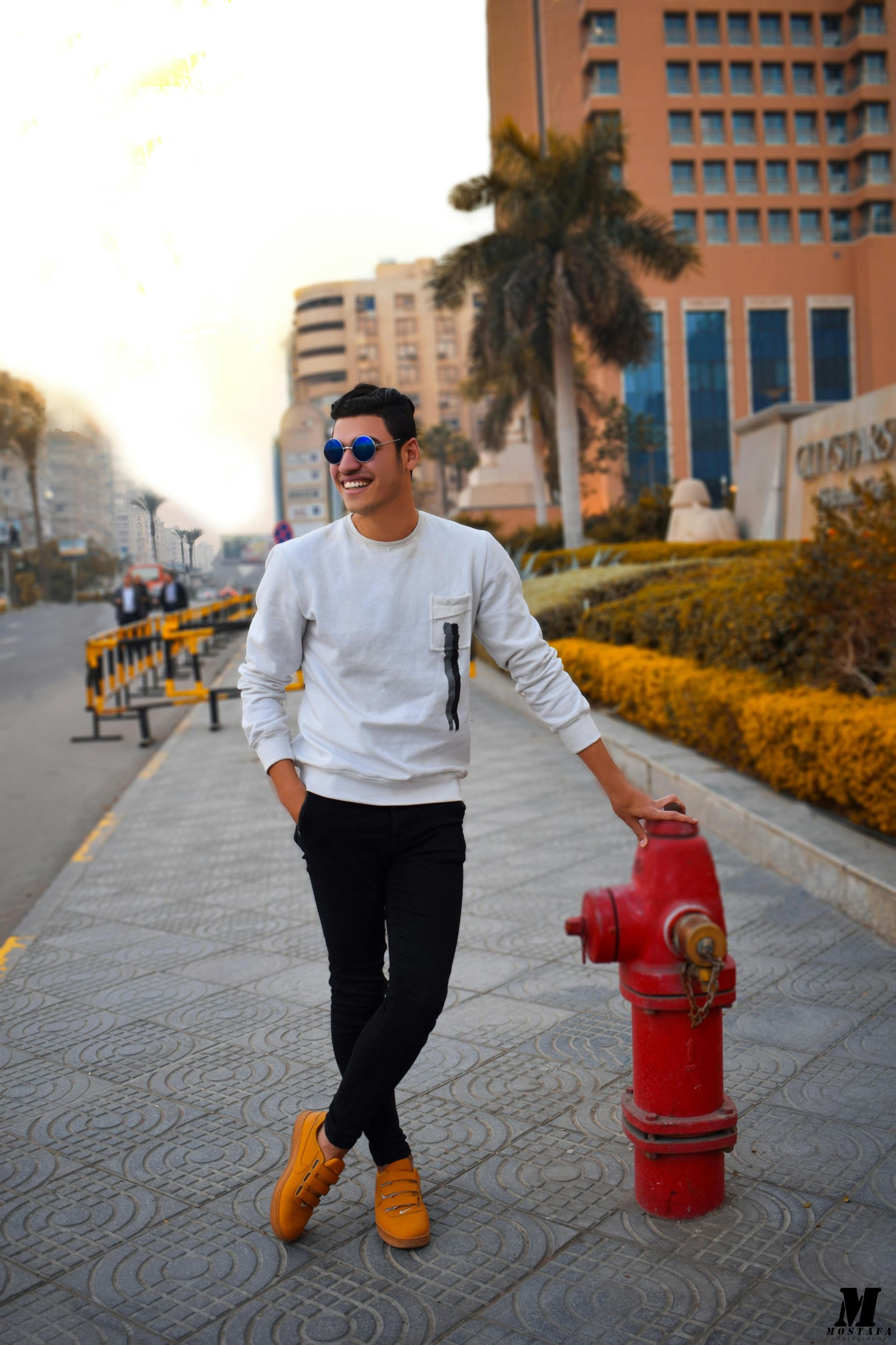 Man in sunglasses leans on a red fire hydrant on a city sidewalk.