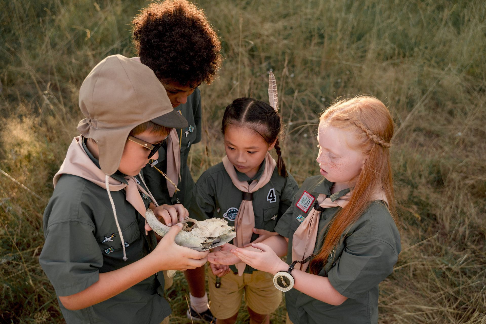 Four scouts in green uniforms studying a map together in a grassy field
