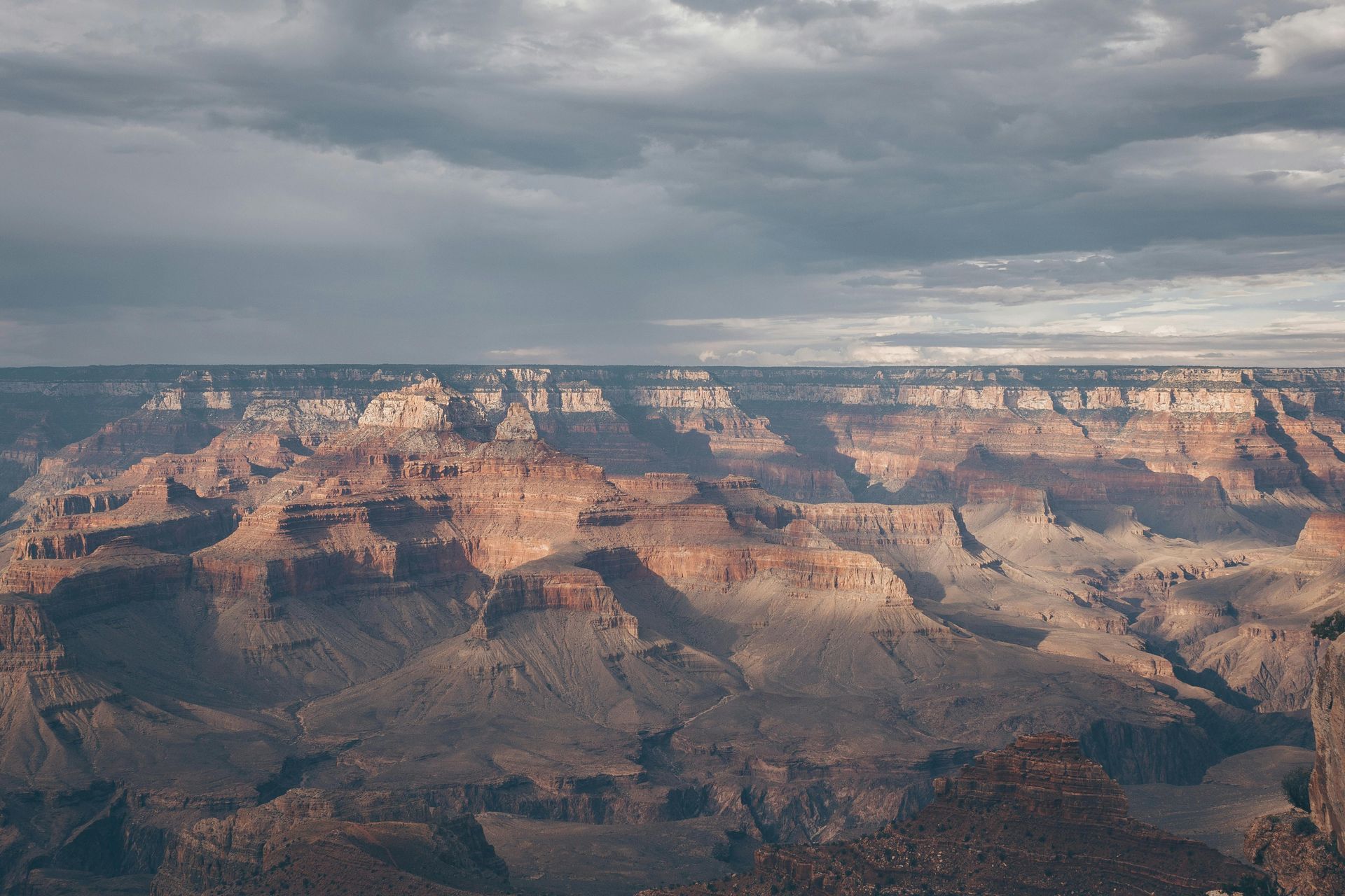 Grand Canyon vista under a stormy sky; canyon walls are lit by the sun.