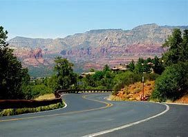 Winding road through a scenic desert landscape with red rock mountains under a clear blue sky.