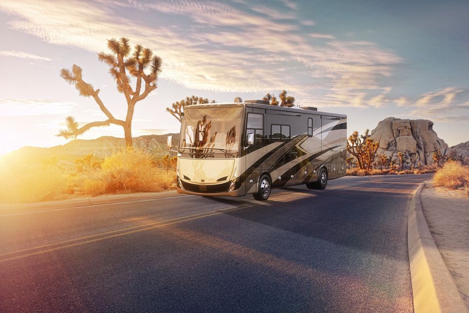 RV driving on desert road at sunset, Joshua trees and rock formations in the background.