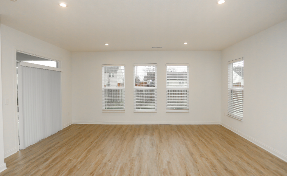 Large living room with hard wood flooring, four windows, and sliding glass door to outside