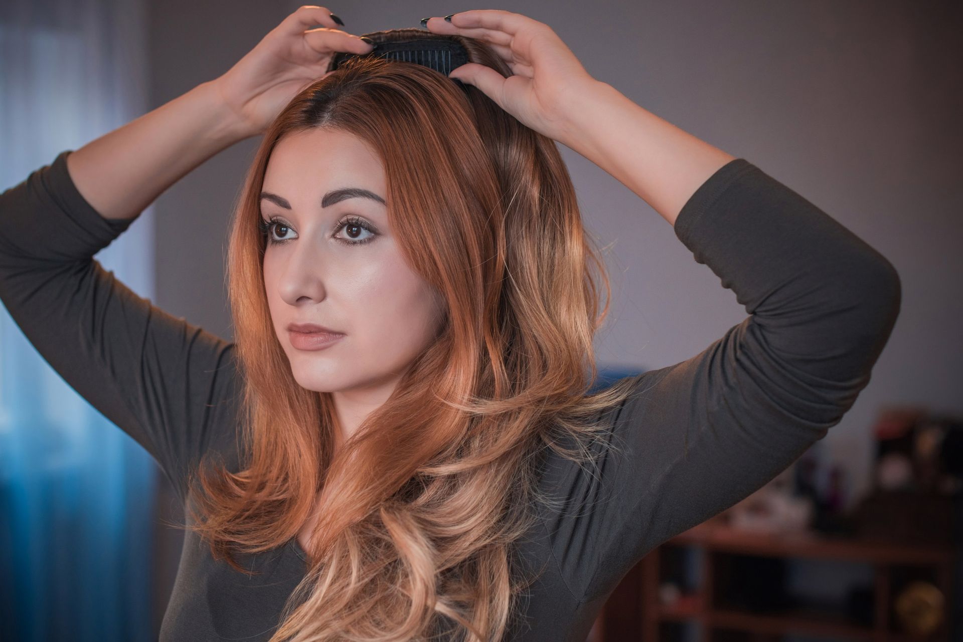 Woman adjusting her long auburn hair with both hands indoors, wearing a dark top Woman adjusting her long auburn hair with both hands indoors, wearing a dark top