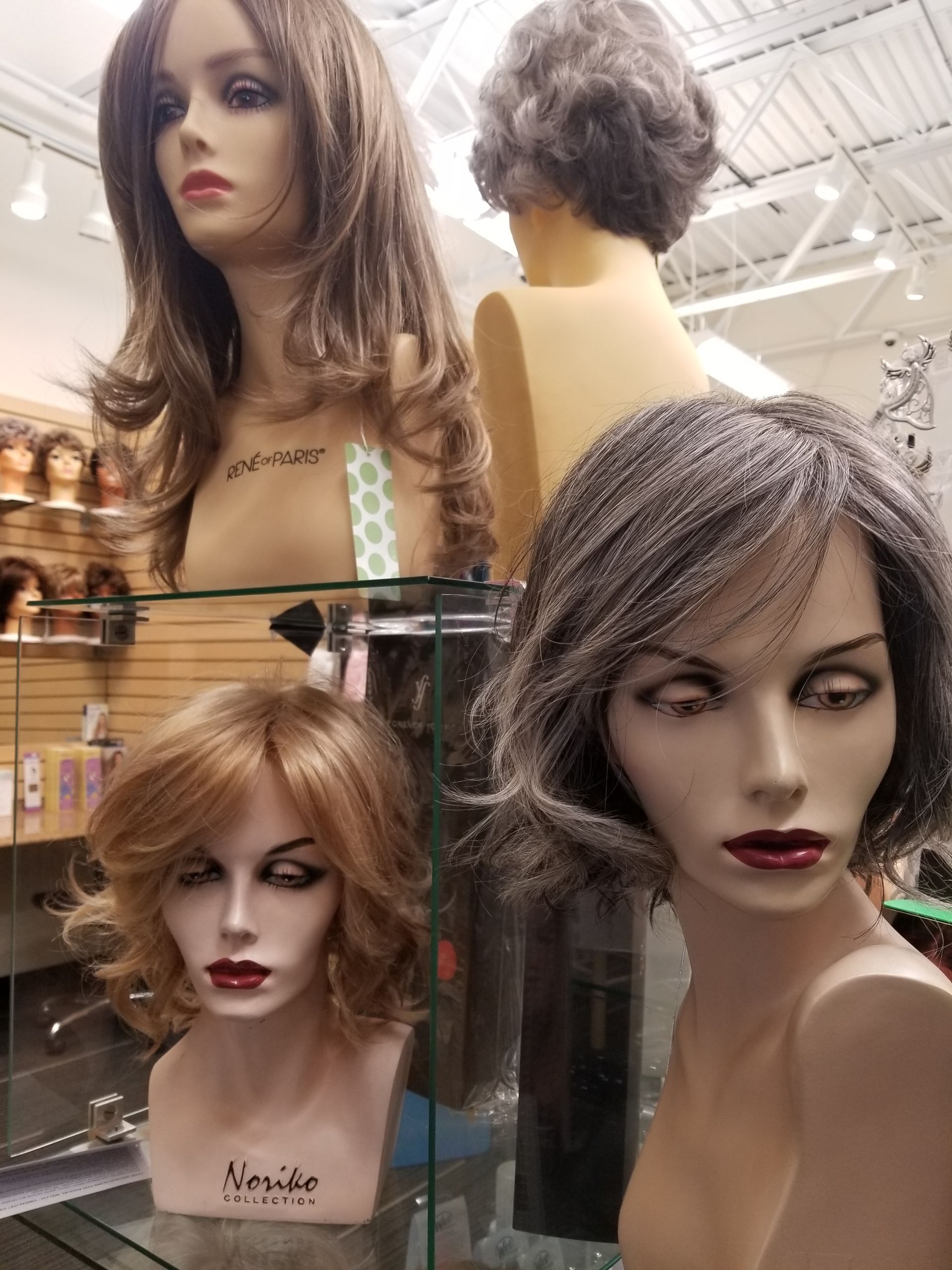 Woman in a turquoise wig poses in front of a shelf of wig displays. Woman in a turquoise wig poses in front of a shelf of wig displays.