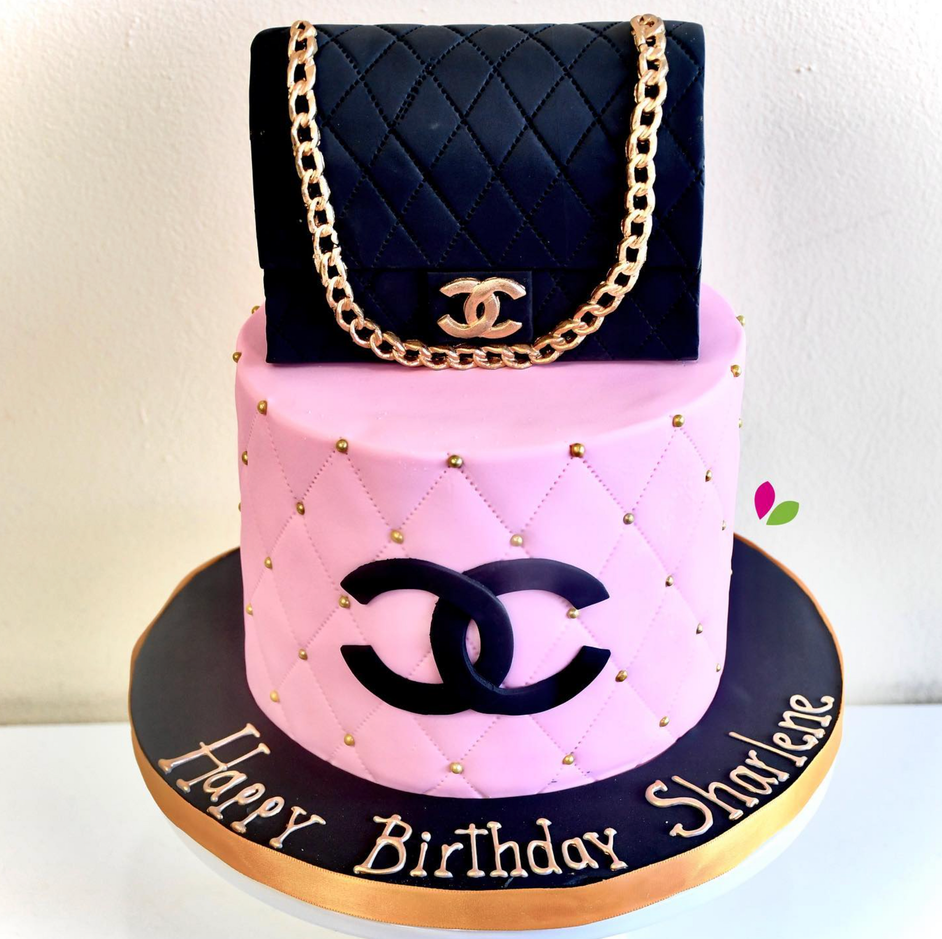 A pink birthday cake with a black chanel purse on top