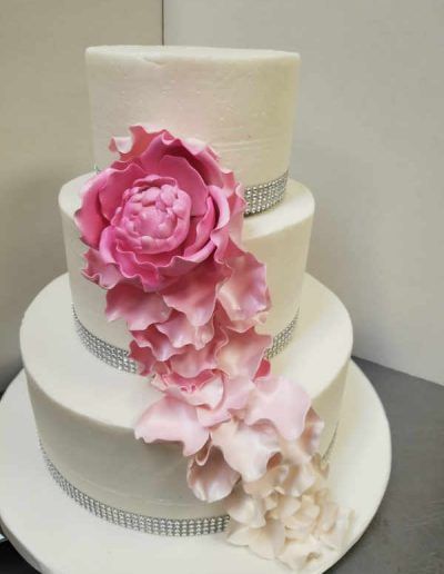 A white wedding cake with a pink flower on top