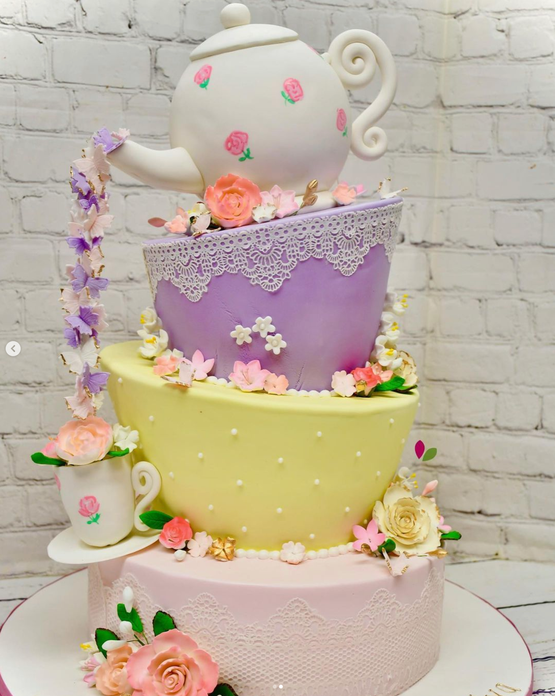 A three tiered cake with a teapot and cups on top.