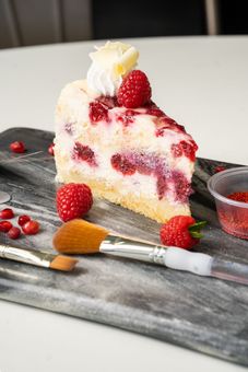 A slice of cheesecake with raspberries and whipped cream on a cutting board.