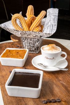 There is a basket of churros and a cup of coffee on the table.
