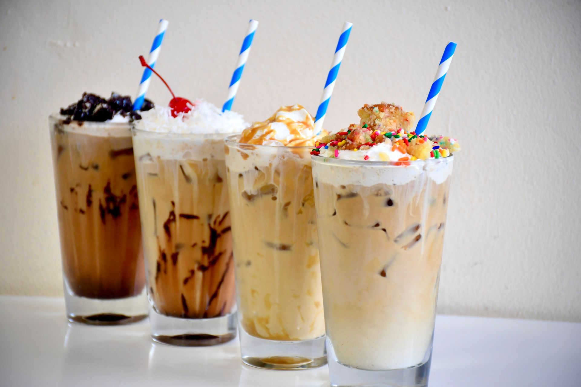 A row of iced coffee drinks with straws on a table.
