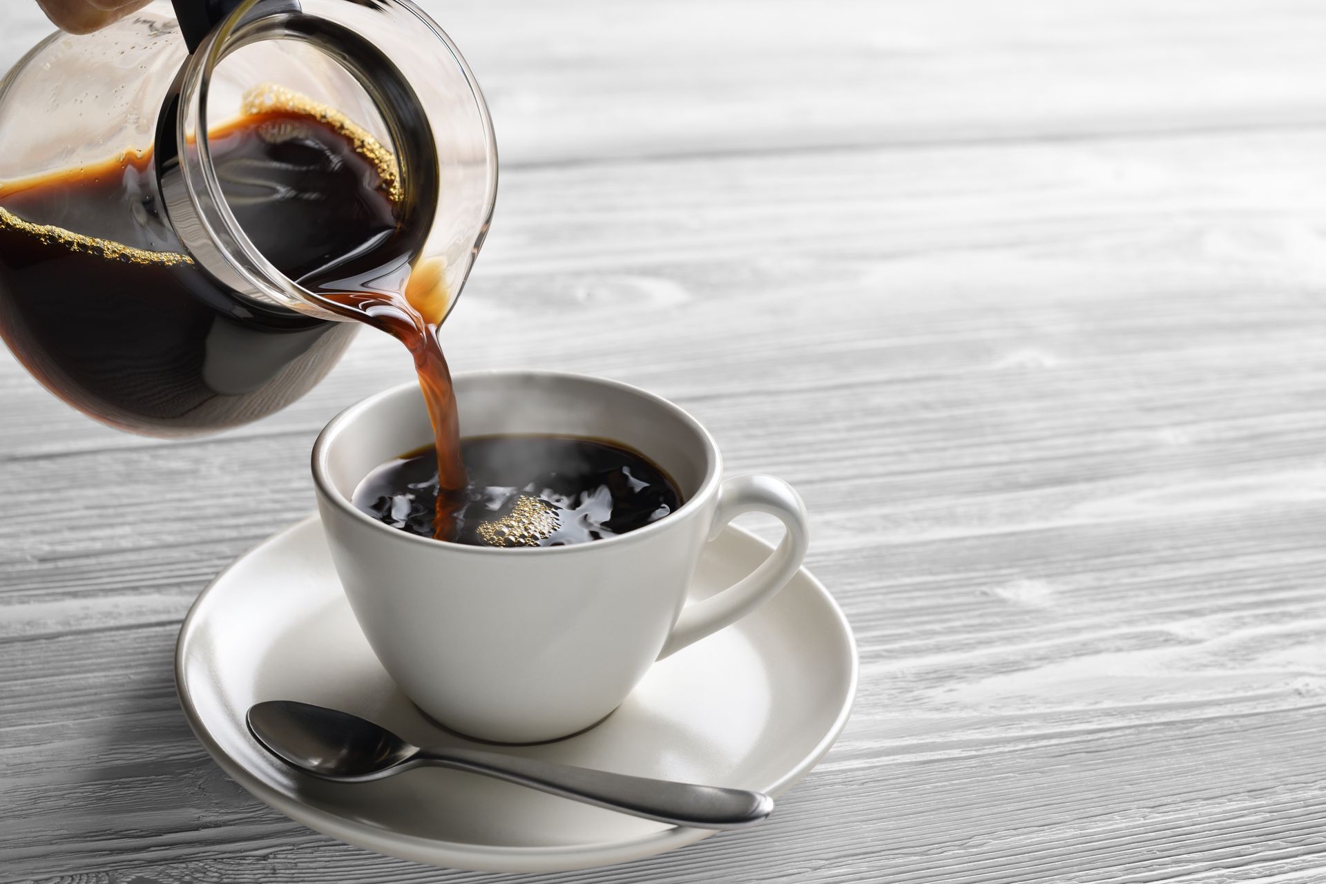 A cup of coffee is being poured from a coffee pot into a cup on a saucer.