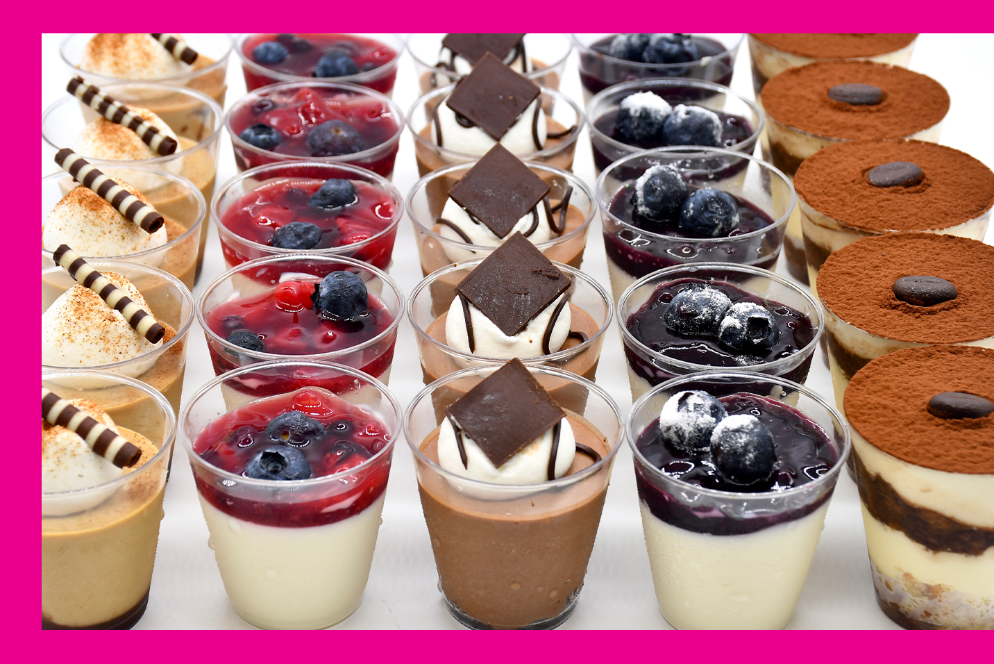 A variety of desserts in plastic cups are lined up on a table.