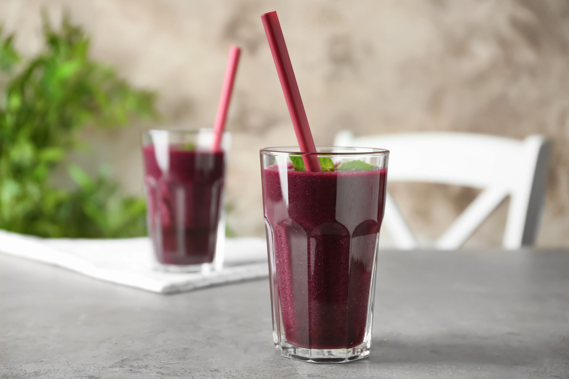 Two glasses of smoothies with red straws on a table.