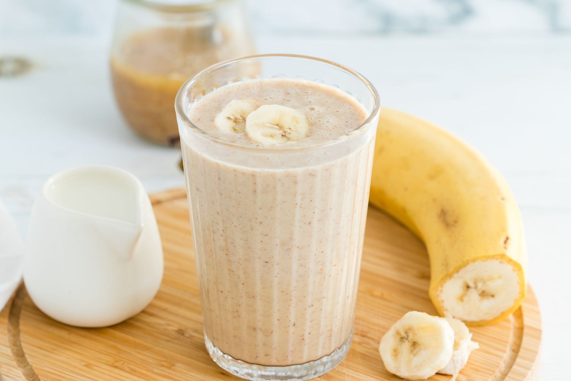 A banana smoothie is sitting on a wooden cutting board next to a banana.